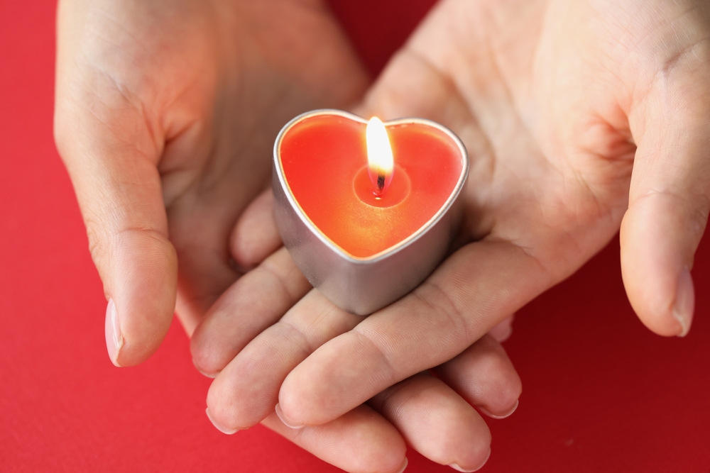 Someone holding a lit heart shaped tea light in their hands