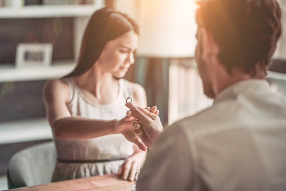 A man holding an engagement ring to a woman as she pushes it away