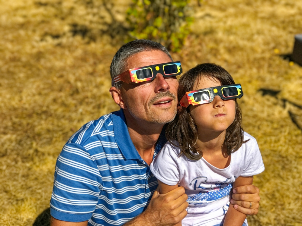 A dad and daughter with solar eclipse glasses on