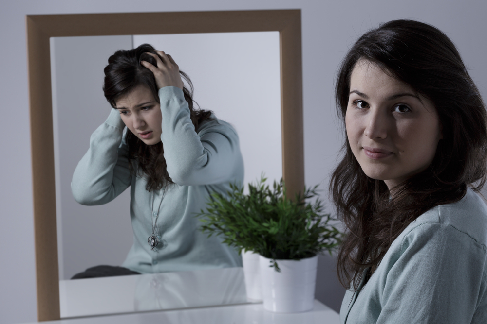 Young woman looking happy and calm, while her reflection shows anxiety and stress