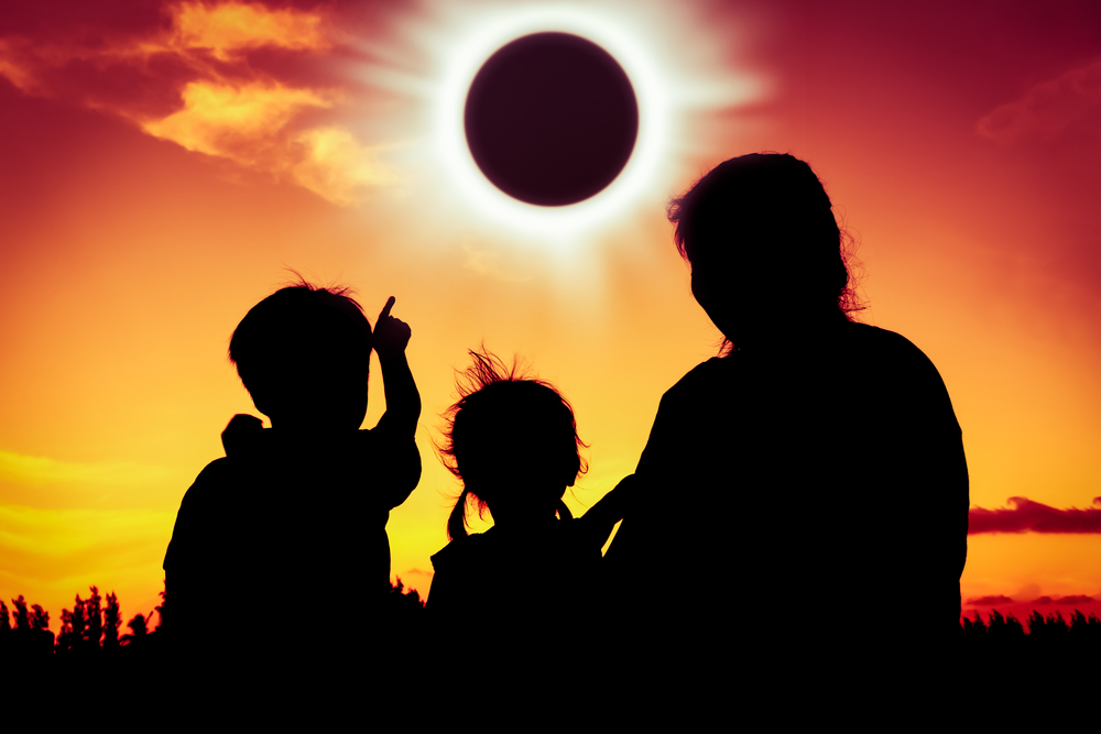 Silhouettes of three people watching a solar eclipse