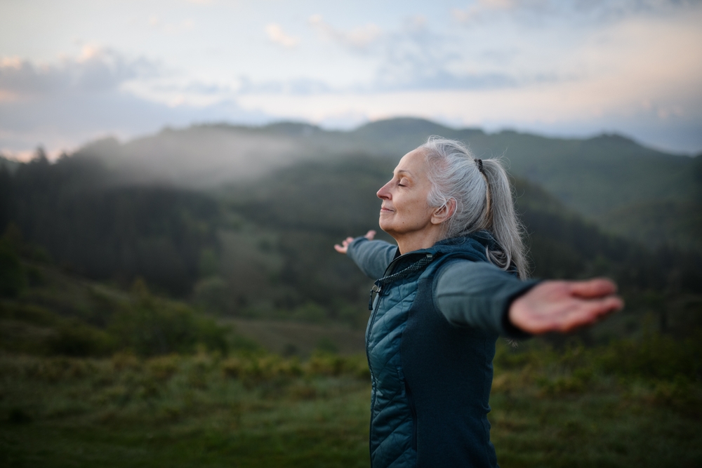 A woman outdoors with her arms stretched out to the side and her eyes closed